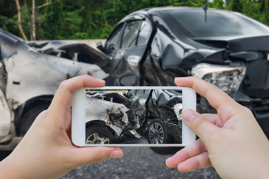 A man taking a photo of the damage to his car after a car accident, fulfilling his post car accident checklist.