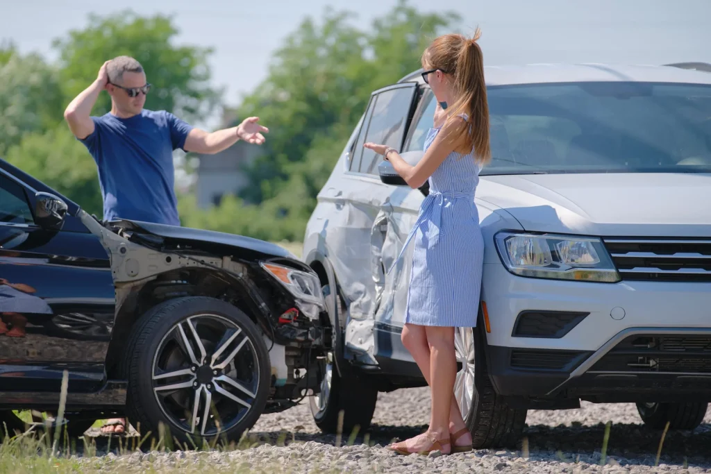 Woman gesturing to a man who is looking at the damage done to an SUV and car after a collision.