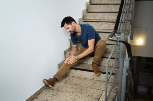 A man who is sitting on the stairs holding his leg in pain.