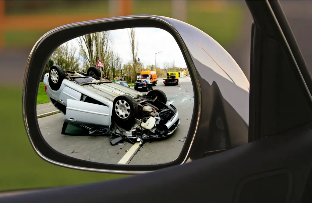Car flipped on road shown in a side mirror.