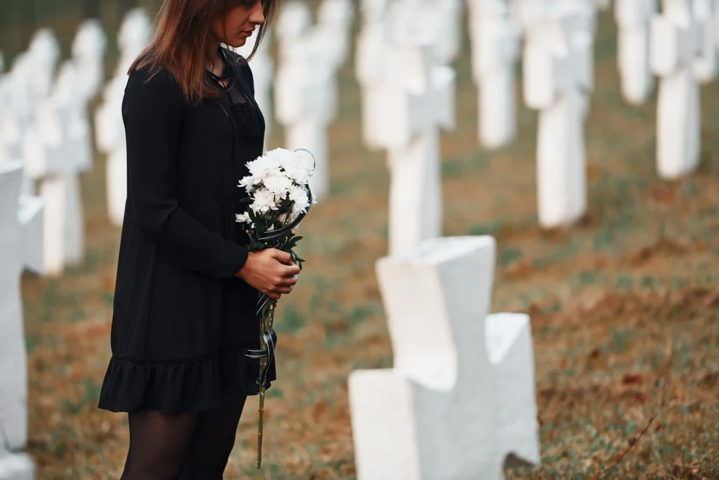 A woman visiting a grave site with a flower bouquet.