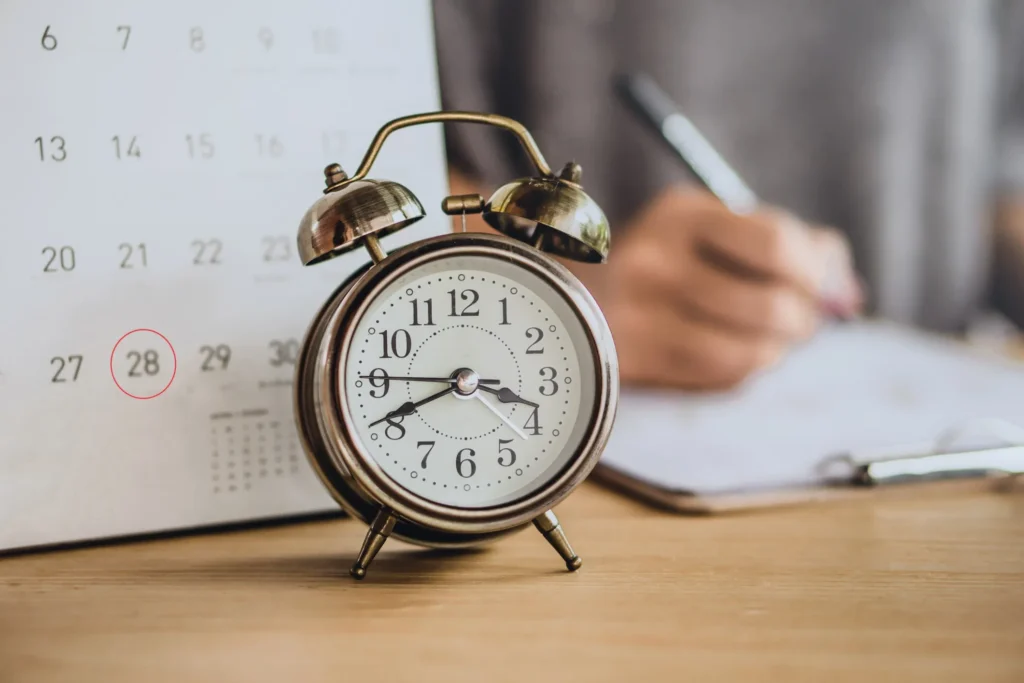 A calendar and clock on a table while a person works in the background.